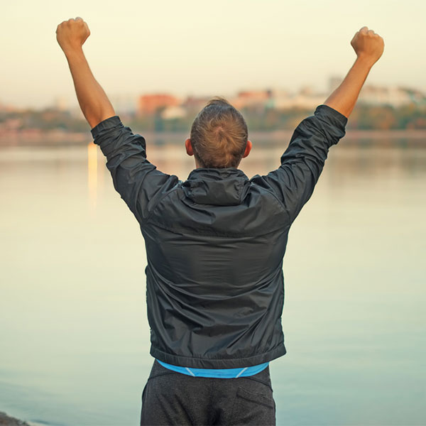 Man holding his fists in the air, standing in front of a lake