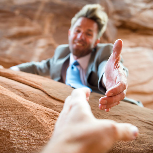 Man in a suit, reaching his hand out to help someone on a cliff